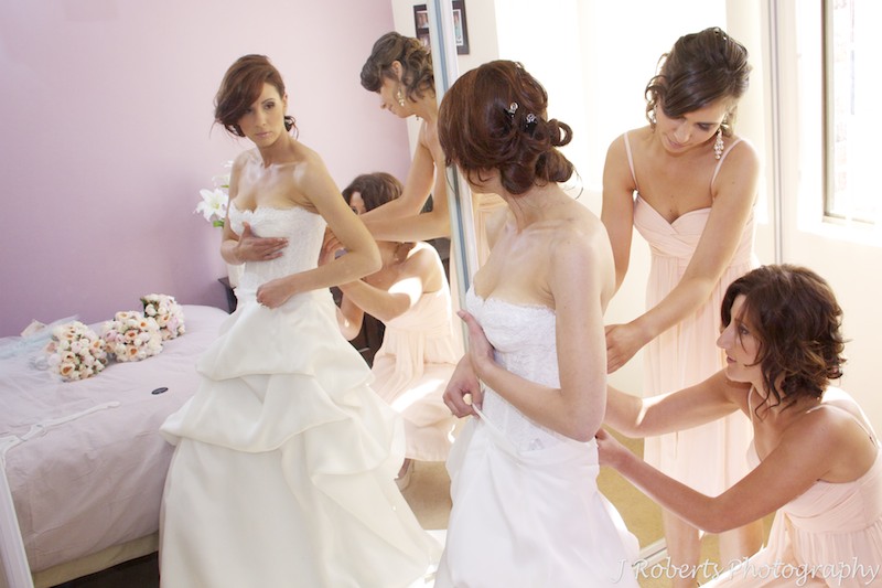 Bride being helped into her dress by bridesmaids - wedding photography sydney